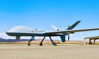 Reino Unido firma contrato para operar nova frota de drones militares Protector RG Mk1 (X @GenAtomics_ASI) Drone militar aparece estacionado em uma base aérea, sob céu claro e ambiente desértico. A aeronave não tripulada exibe design robusto e moderno, com asas longas e trem de pouso visível.